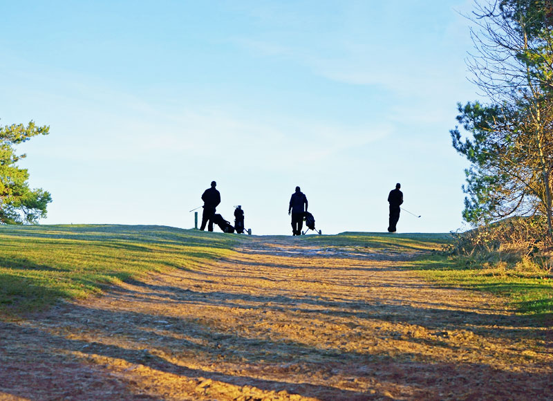Three people playing Golf on the top of a hill.